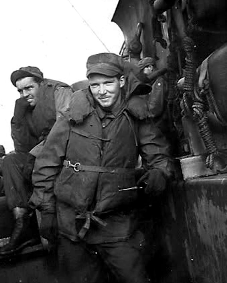 Alan Thevenet in a life belt and field jacket aboard a troop transport during the Second World War, smiling at the camera